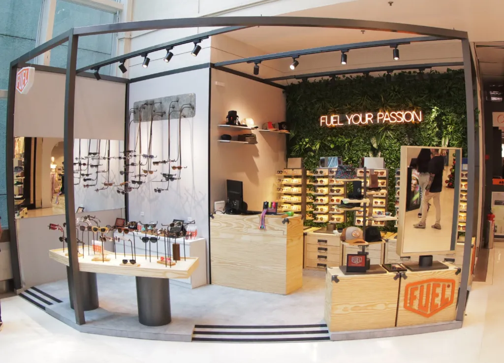 Quiosque Fuel Eyewear em shopping com design moderno, parede verde, expositores de óculos premium e atendimento consultivo, exemplo de experiência imersiva no varejo óptico