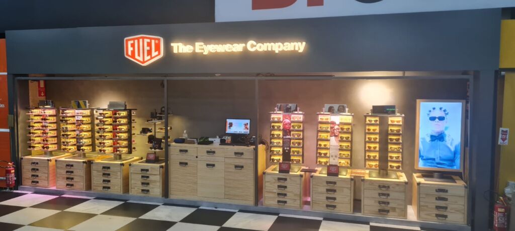 Quiosque da Fuel Eyewear no aeroporto de congonhas com expositores em madeira, iluminação quente e vitrines modernas