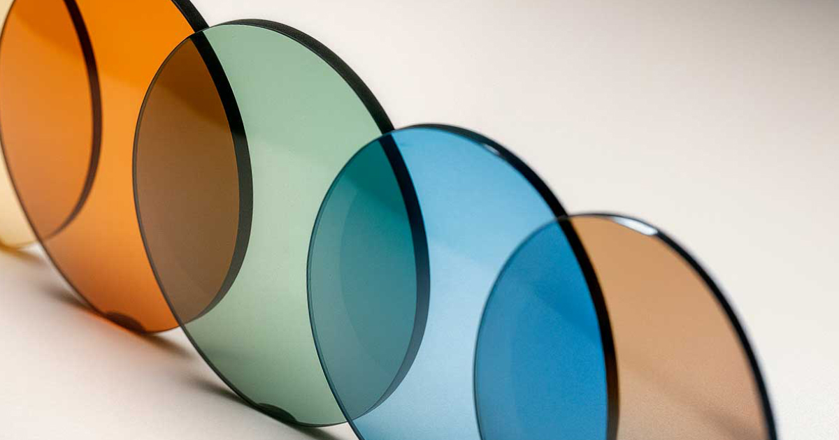 Sequência de lentes redondas para óculos dispostas lado a lado em fundo neutro, exibindo variações de cores e tonalidades como âmbar, verde, azul e castanho.