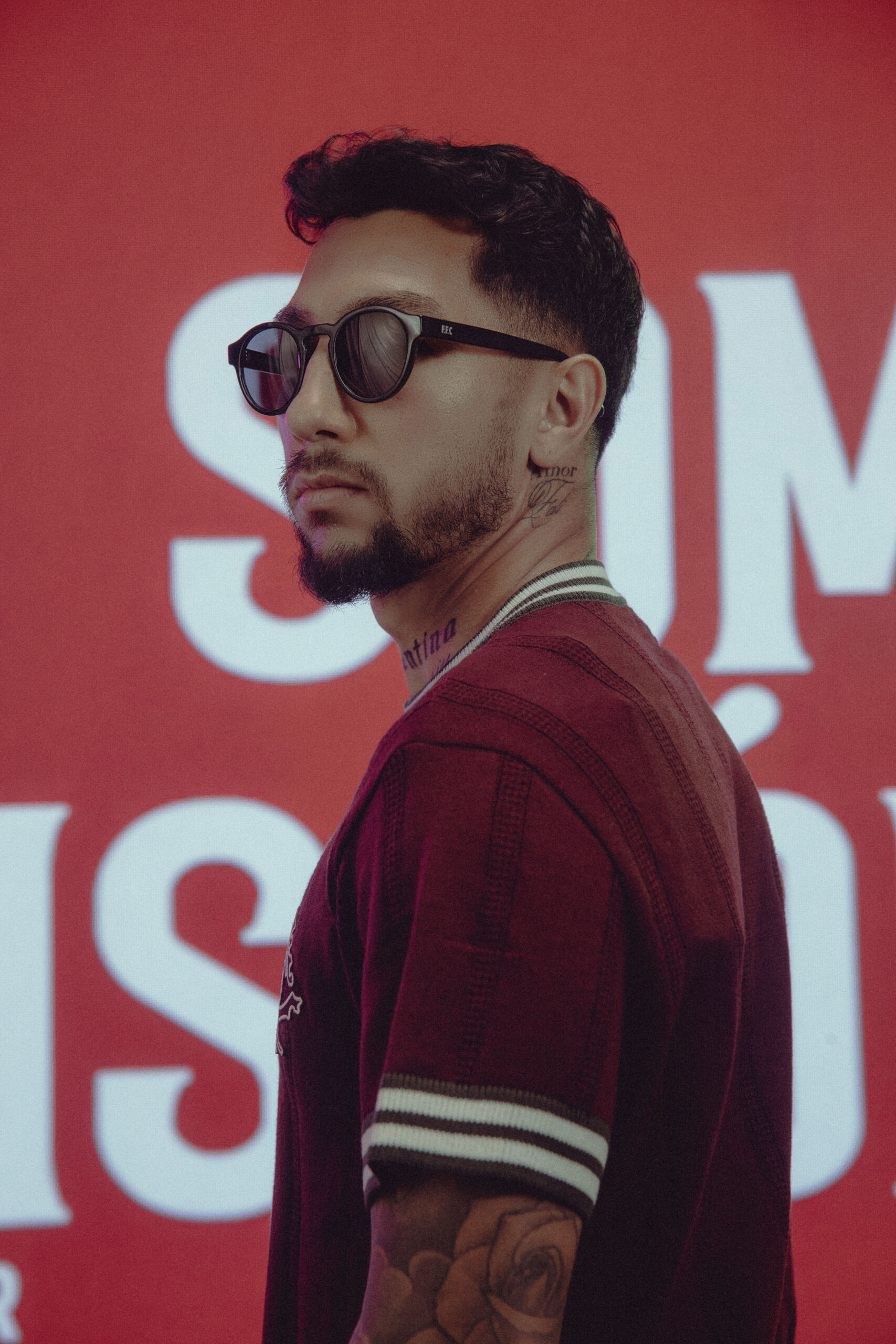 Modelo masculino de perfil a usar óculos de sol redondos e camisola grená do Fluminense, com a frase 'Nós Somos a História' estampada no fundo