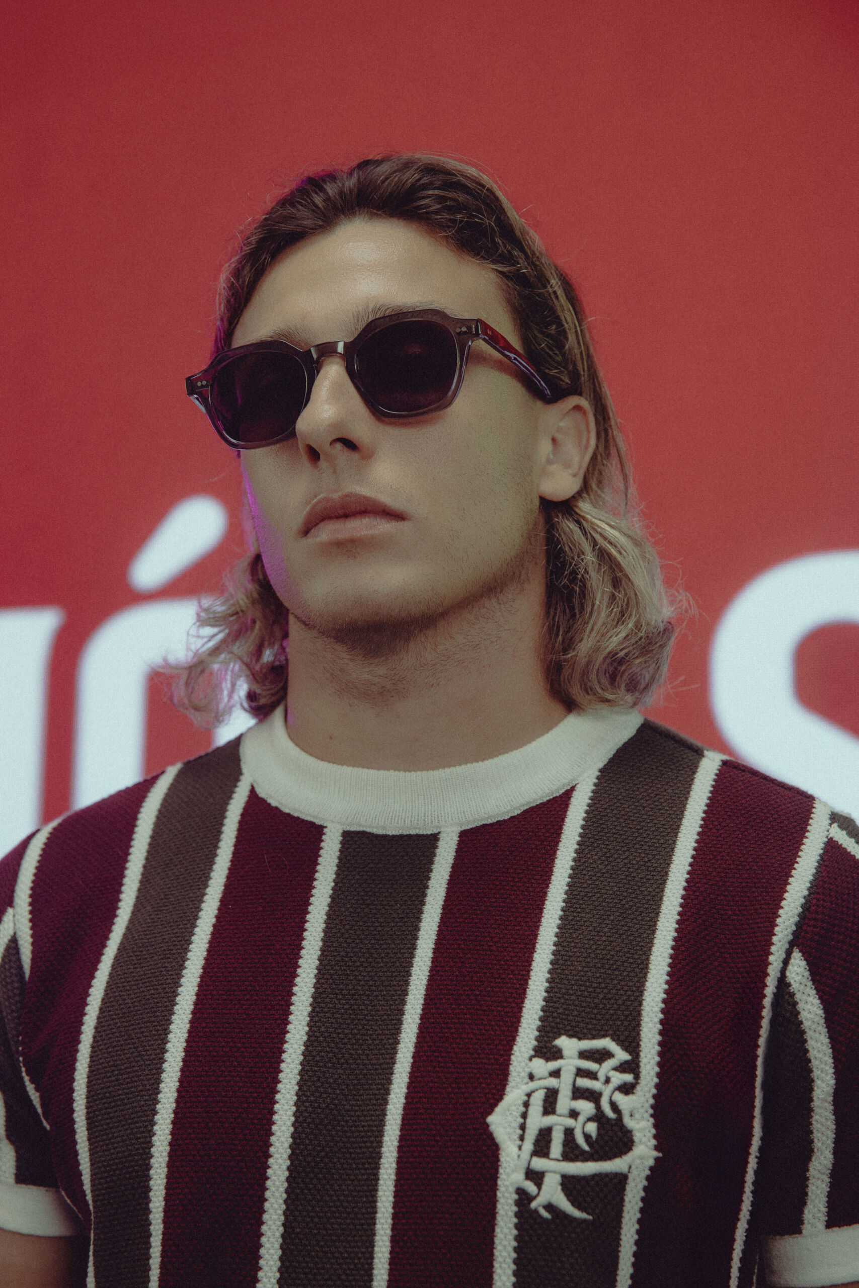 Modelo masculino de perfil a usar óculos de sol redondos e camisola grená do Fluminense, com a frase 'Nós Somos a História' estampada no fundo