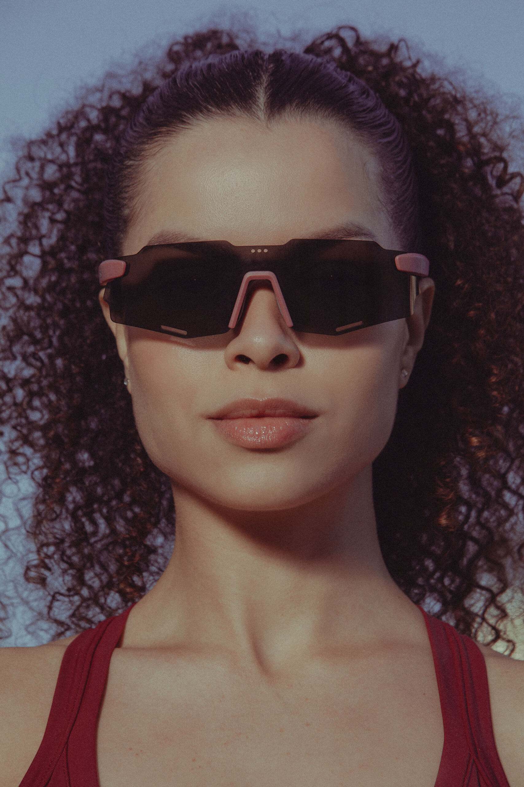 Primeiro plano de uma mulher de cabelo encaracolado a usar óculos de sol esportivos estilo máscara com pormenores em rosa